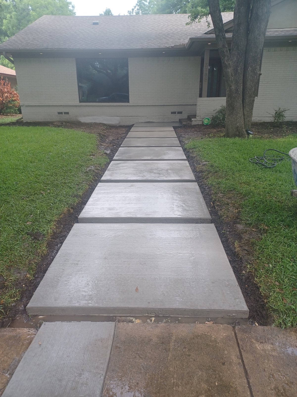 Concrete sidewalk pathway leading to a single-story ranch house with white siding and large dark windows