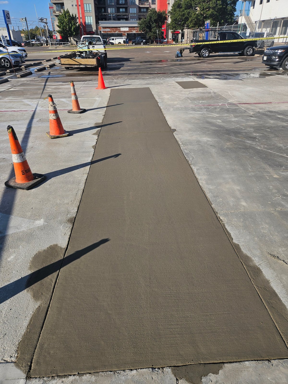 Freshly poured concrete strip on urban street marked with orange safety cones during construction