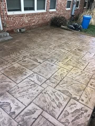 Stamped concrete patio with geometric patterns in front of brick house with windows and blue trash bin