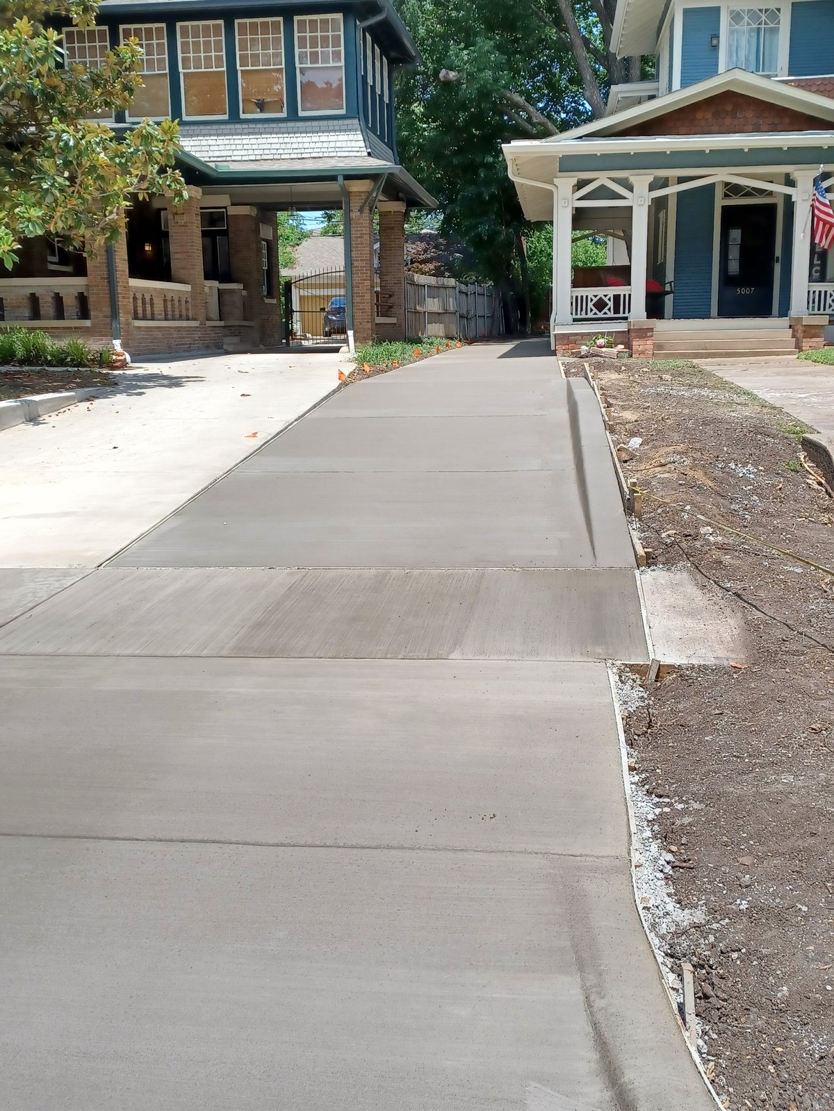 Newly poured concrete sidewalk between two historic residential houses with brick and wooden architectural details