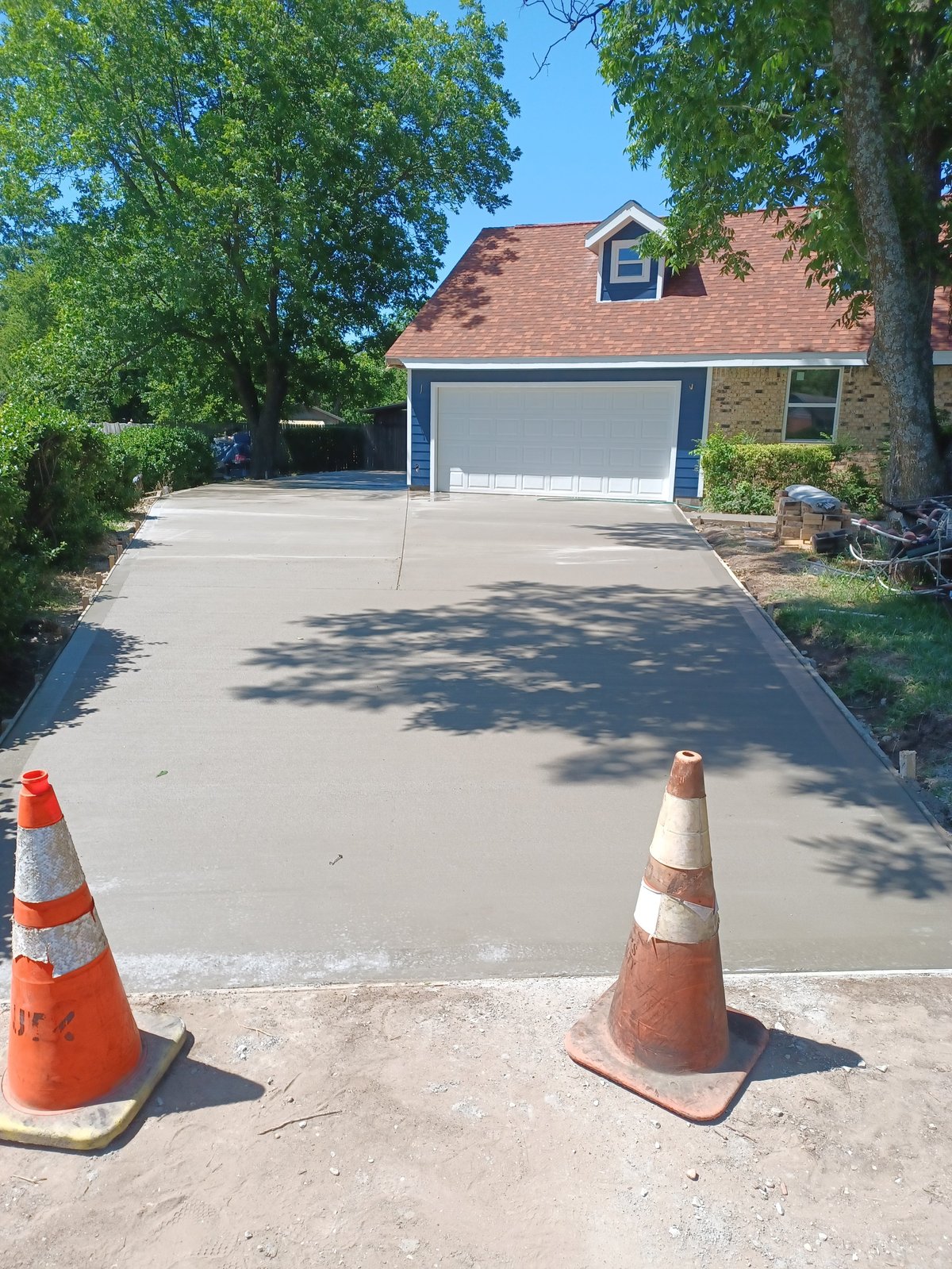 Freshly poured concrete driveway in front of a brick house with orange traffic cones marking the wet surface
