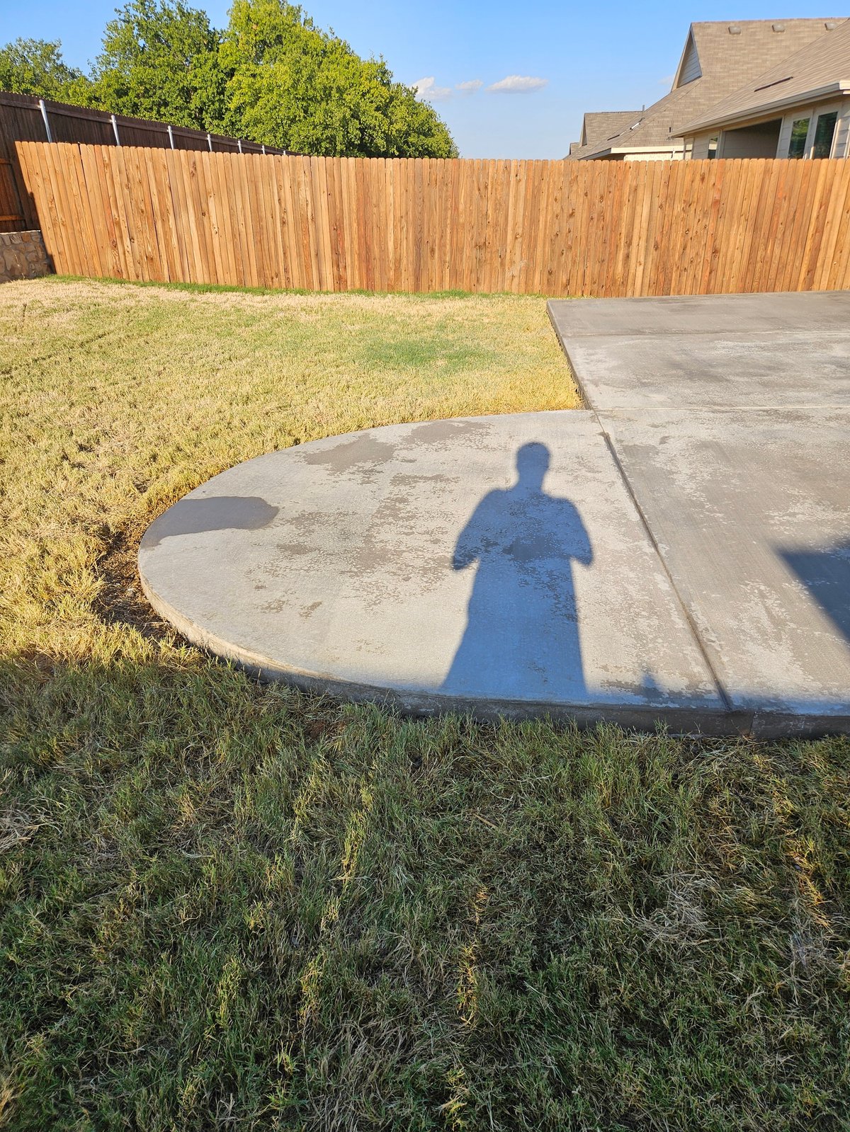 Tall cedar-stained wooden fence enclosing a backyard with a curved concrete patio and green lawn